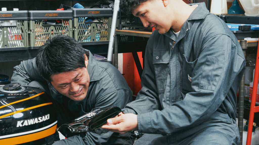 ここからは一気に組み上げフェーズ。 リアフェンダー、フロントフェンダー、テールカウル、テールランプ、ウインカー、シート…… 次々にZ2パーツを装着していく。 岡野はサイドカバーにエンブレムを慎重に貼り付ける。